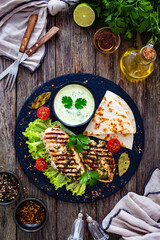 Grilled chicken breast, pita bread and fresh vegetables on wooden table
