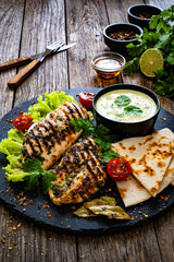 Grilled chicken breast, pita bread and fresh vegetables on wooden table
