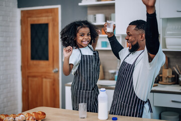 Father-daughter bond in kitchen, laughing, cheering milk competition, creating cherished memories.