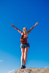 Woman standing on cliff with open arms against blue sky- freedom,  achievement,