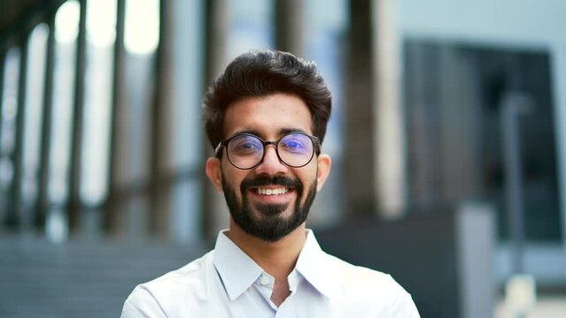 Close up portrait of a young businessman in a shirt and glasses smiling and looking at the camera. Handsome male posing standing on the street in front of an office building. Head shot of the manager