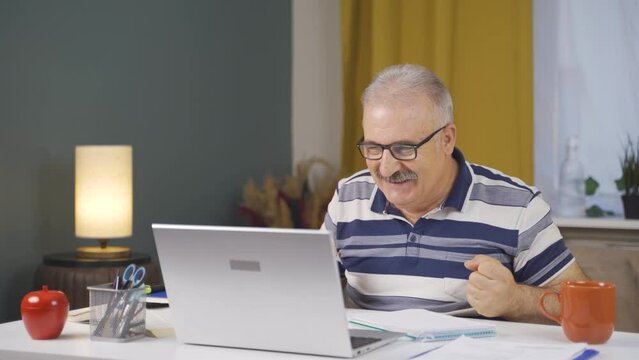 Home office worker old man rejoices at what he sees on the laptop.