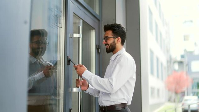 Young bearded businessman unlocking door using mobile phone application. Unlocks a modern office building. Scanning open smartphone with mock up screen app. Smart electronic locks with keyless access