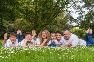 Fototapeta premium Happy big family. Mom, dad and 4 sons of different ages lie on the grass among the daisies. The youngest is 1 year old