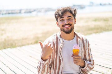 Handsome Arab man with a cornet ice cream at outdoors pointing to the side to present a product