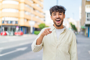 Young Arabian handsome man at outdoors surprised and pointing front