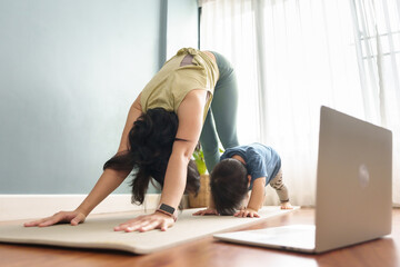 Asian mother and little son doing fitness exercise on yoga mat. Sporty Family standing in Downward...