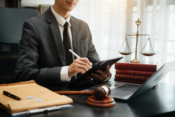 justice and law concept.law theme wooden desk, books, balance. Male judge in a courtroom the gavel,working with digital tablet computer on table. © laddawan