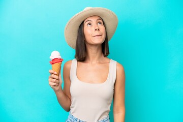 Young caucasian woman holding an ice cream isolated on blue background and looking up