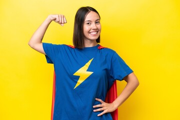 Young caucasian woman isolated on yellow background in superhero costume and doing strong gesture © luismolinero