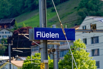 Blue and white sign at railway station of Swiss village Flüelen on a sunny spring morning. Photo taken May 22nd, 2023, Flüelen, Canton Uri, Switzerland.