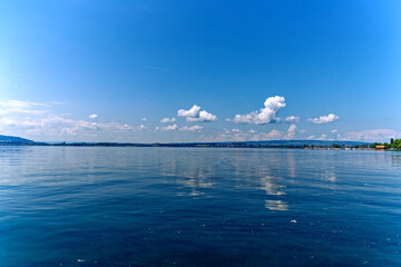Scenic view of lakeshore of Lake Zug with fluffy clouds at City of Zug on a sunny spring day. Photo...