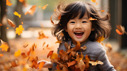 Cute asian child playing with autumn leaves in the park 
