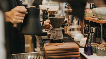 Professional barista making filtered drip coffee in coffee shop. Close up of hands barista brewing a drip hot espresso, pour over coffee with hot water and filter paper in cafe.