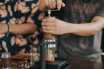 Fototapeta na wymiar Professional barista making fresh coffee from ARAM espresso machine. Close up of hands barista brewing dirty coffee by handmade coffee machine in counter coffee shop.