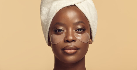 Face of black girl in hair towel with eye patches on skin.