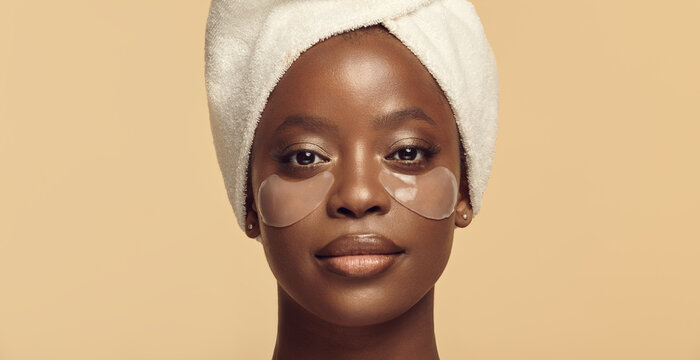 Face of black girl in hair towel with eye patches on skin.