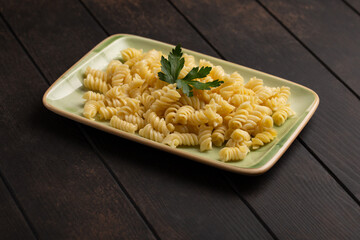 Fresh cooked fusilli pasta on a plate on wooden background.
