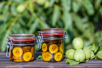 Tincture of green walnuts in a glass jars on a wooden table in a summer garden. Sliced unripe...