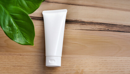 Blank white plastic cosmetics tube and green leaf on wooden board. Skincare, beauty treatment, spa...
