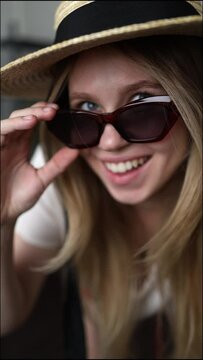 a girl in a straw hat and sunglasses poses for the camera and laughs. female smile with beautiful teeth. the girl takes off her glasses and laughs at the camera. vertical video