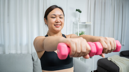 Fototapeta na wymiar Determined Young Asian healthy woman losing weight training in living room at home and exercising with dumbbells fitness exercises Healthy lifestyle