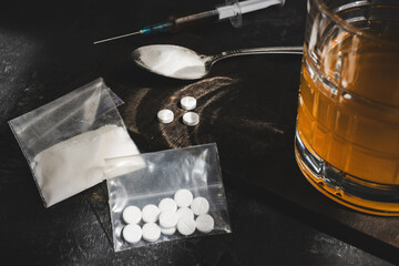 Alcohol drink in a glass, syringe with a dose of drugs, white pills and narcotics powder in a transparent bag on dark background. Concept of addiction, abuse and bad habits