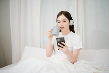 Beautiful woman has woken up on a white bed and holding coffee in the morning at home in morning