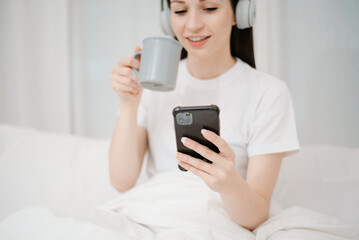 Beautiful woman has woken up on a white bed and holding coffee in the morning at home in morning