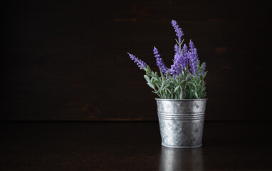 Photo of tin bucket with artificial lavender on dark wooden background.