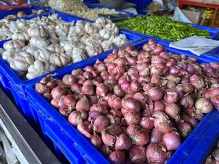 Pile of garlic and onion on a blue plastic tray being displayed in a traditional market for sale