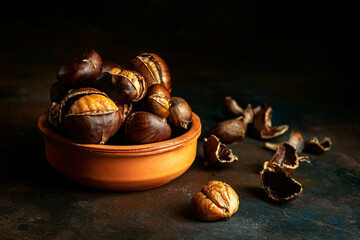 Roasted chestnuts in a clay bowl on black background. Traditional food concept. Dark low key photo....