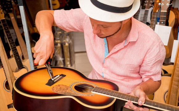 Young musician changing strings on a classical guitar in a guitar shop