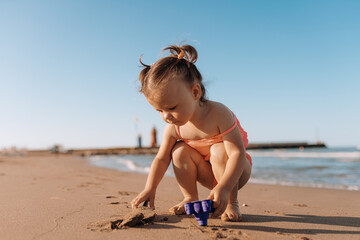 Fototapeta premium little child sea, girl in swimsuit joyful plays on the beach