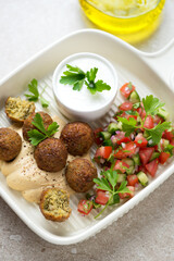 Falafel with hummus, tomato salsa and yogurt in a beige serving tray, vertical shot, middle close-up