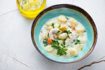 Creamy chicken gnocchi soup in a turquoise bowl, horizontal shot on a white granite background, selective focus