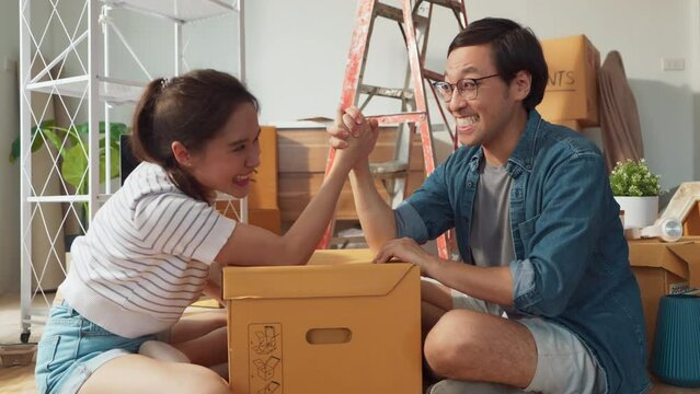 Young cheerful asian adult couple having fun while arm wrestling for dominance in the house.Home renovate decision organize house arrangement with fun and humor family concept