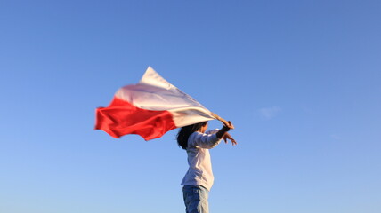 a girl wearing a white t-shirt holding an Indonesian flag against a clear blue sky as a background. independence day concept
