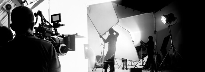 Silhouette of video production behind the scenes or B roll or making of TV commercial movie that film crew team lightman and cameraman working together with director in big studio with pro equipments - obrazy, fototapety, plakaty