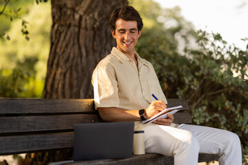 Fototapeta premium Cheerful young man attending webinar while resting at park