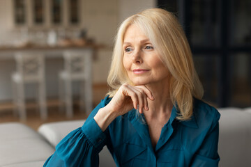 Closeup portrait of dreamy mature woman relaxing at home, female sitting on comfortable couch and looking away