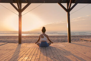 Woman on the beach at sunrise in meditation pose