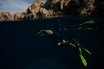 Unrecognizable man swimming underwater in mountainous bay