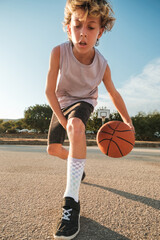 Concentrated boy dribbling basketball on sports ground