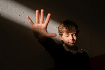 Boy with closed eyes showing stop gesture to sudden sunbeam