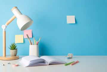 Study corner presented in side view shot with school supplies, pencil stand, flowerpot, adhesive tape, pens, lamp, book sticky notes on a blue wall. Empty space invites text or promotional content