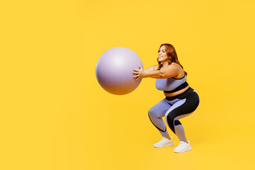 Fototapeta na wymiar Full body side view young chubby plus size big fat fit woman wear blue top warm up training hold in hands fit ball do squats isolated on plain yellow background studio home gym. Workout sport concept.