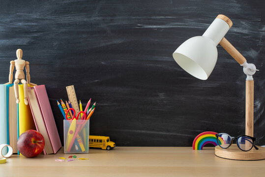 Get inspired by this school-oriented setup: side view photo of desk essentials, stationery, books, lamp, mannequin, glasses, apple and more against chalkboard backdrop, offering space for text or ads