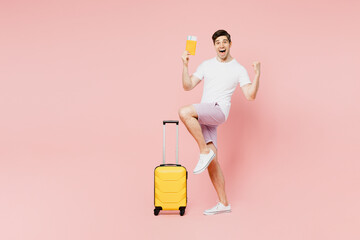 Traveler man wear summer casual clothes hold suitcase do winner gesture isolated on plain pink background studio. Tourist travel abroad in free spare time rest getaway Air flight trip journey concept