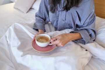 Crop female drinking coffee in bed